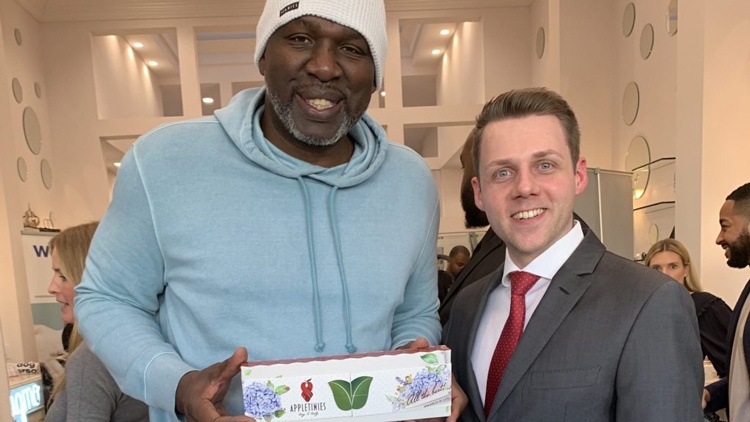 Basketballstar Olden Poylnice hält eine Packung Appletinies. Neben ihm steht Lukas Wilfling.