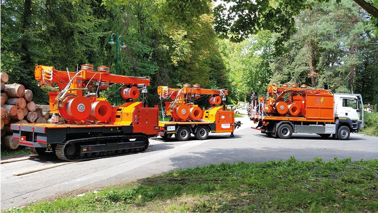 Drei Forstmaschninen fahren auf einer Straße, im Hintergrund stehen Bäume