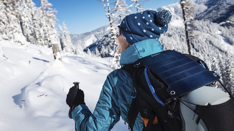Warm angezogene Frau mit Rucksack und Wanderstock in winterlicher Berglandschaft