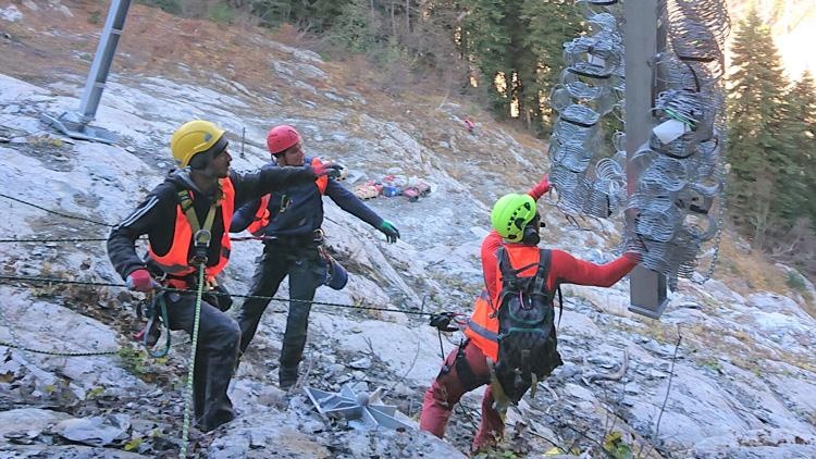 Drei Personen mit Schutzkleidung in gebirgigem Gelände